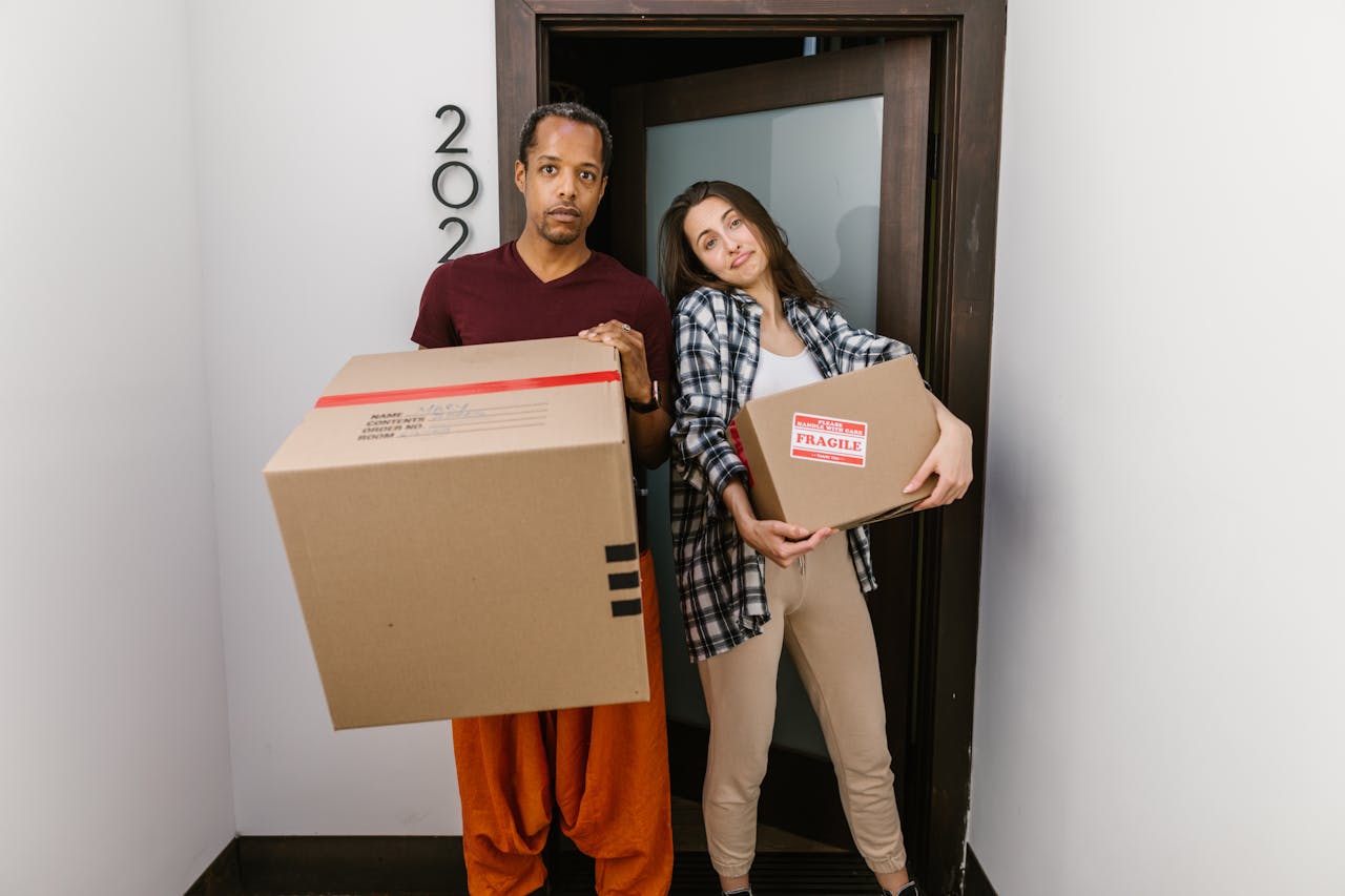 Couple carrying moving boxes at their flat doorway